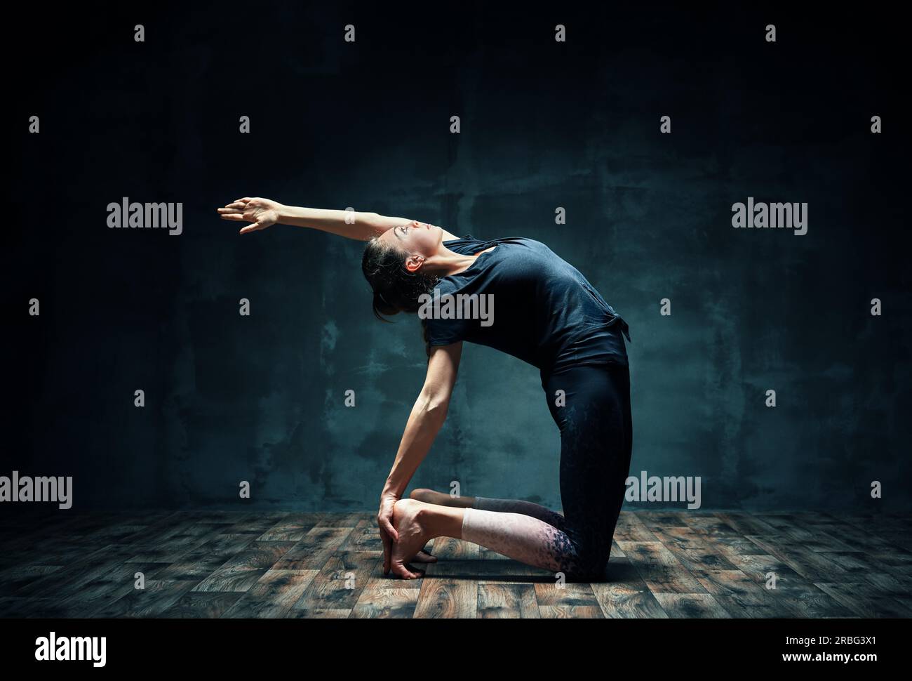Young attractive woman practicing yoga doing half camel pose in dark room. Ardha Ushtrasana exercise. balance and health concept Stock Photo