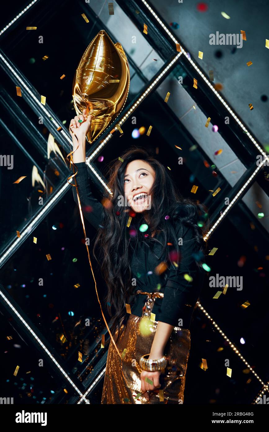 Pretty happy asian woman having fun and dancing at party holding golden balloon. Celebration concept Stock Photo