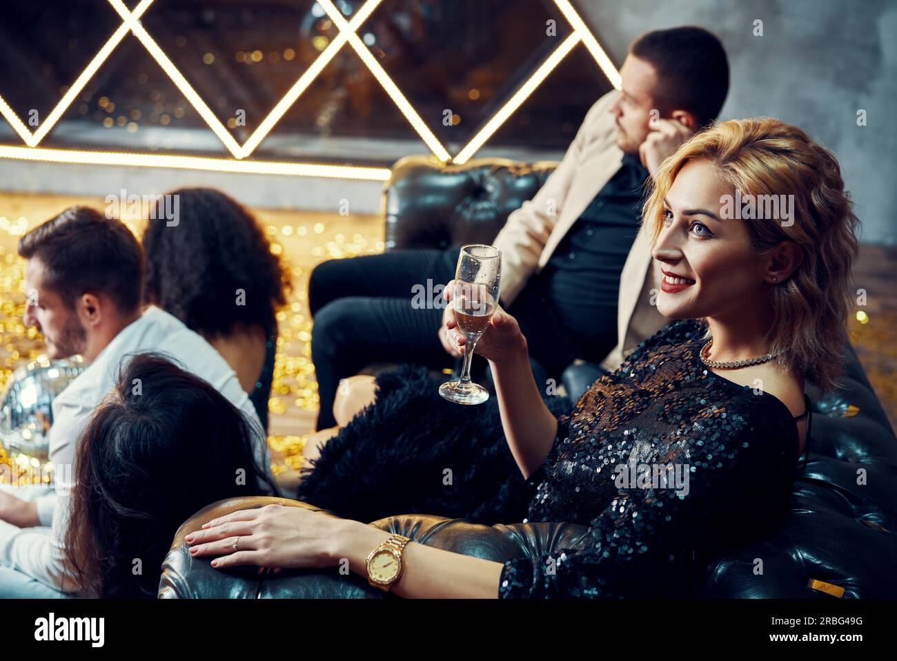 Diverse group of young friends hang out and drink champagne at night club. People enjoy party and have fun concept Stock Photo