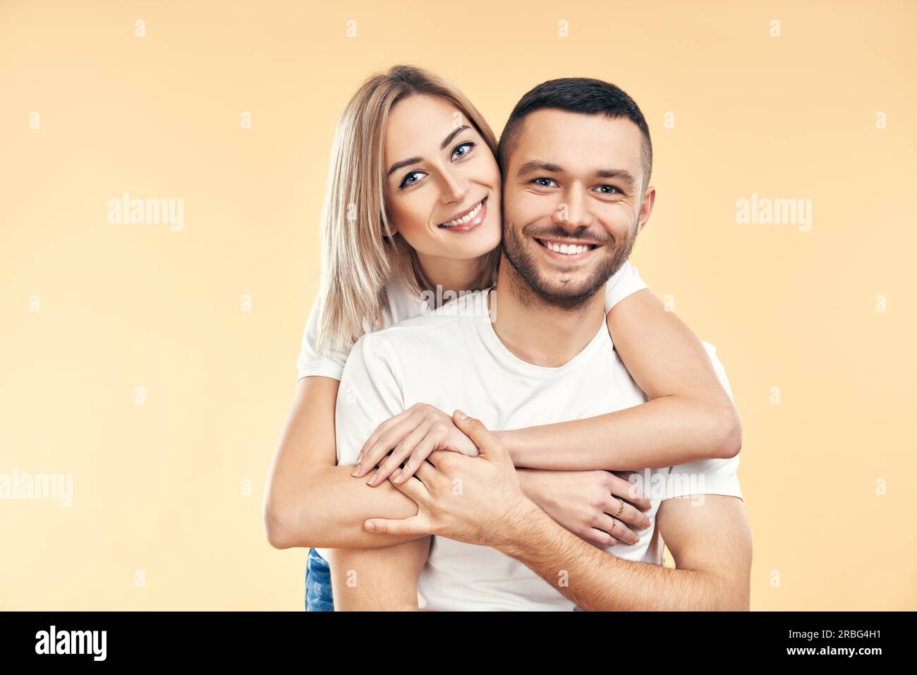 Happy smiling couple in love on beige background. Man carrying his girlfriend piggyback. Love, romance, fun concept Stock Photo