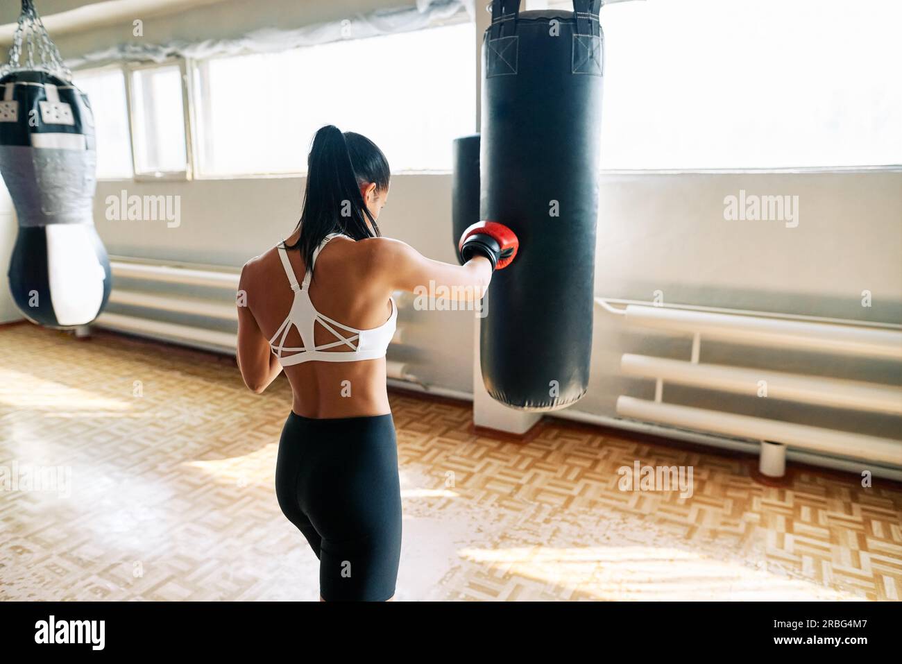 Back view of female boxer hitting a huge punching bag at fitness gym