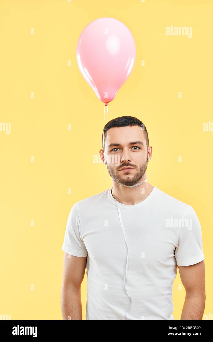 Weird young man with pink air balloon on his neck over yellow studio background Stock Photo