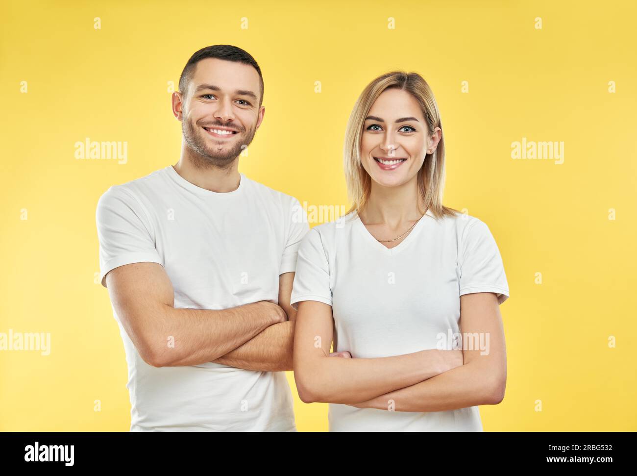 Young happy couple with arms crossed over yellow background. Smiling man and woman posing in studio Stock Photo