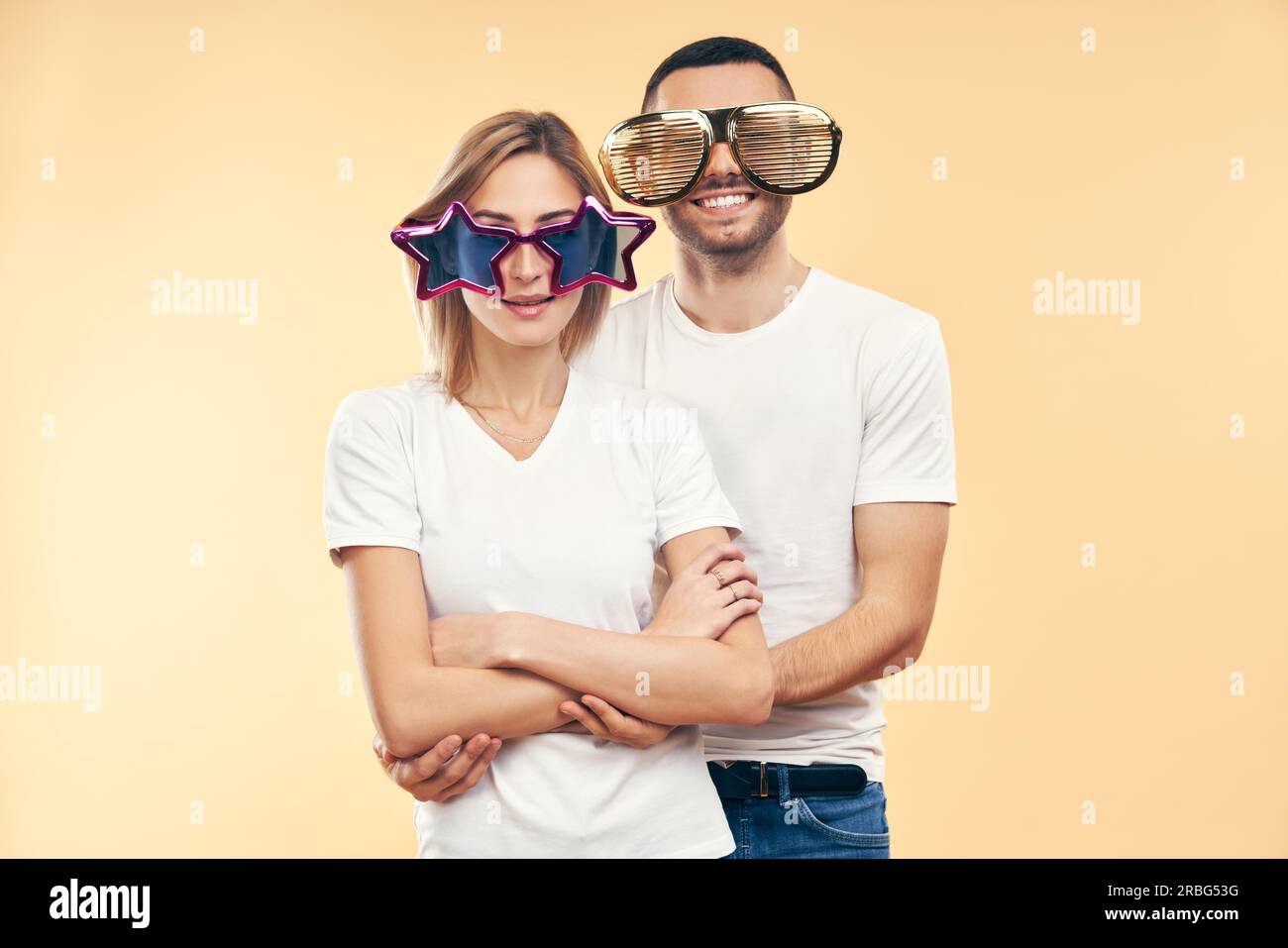 Young happy couple in funny party glasses on beige background. Fun concept Stock Photo