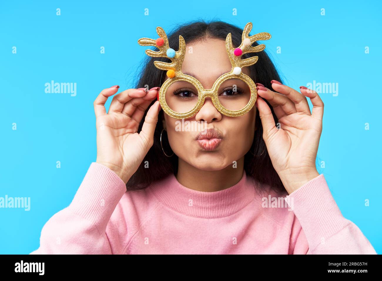 Pretty woman in funny party glasses send air kiss over blue background. Fun concept, carnival, masquerade accessory Stock Photo