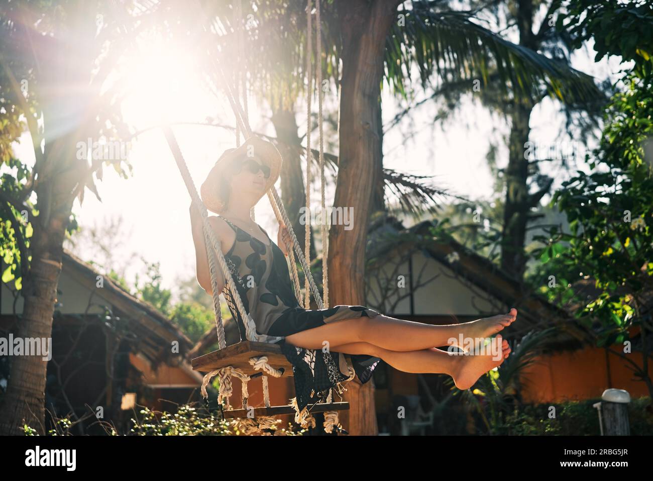 Happy barefoot girl on swing in sun light at tropical island. Carefree woman Stock Photo