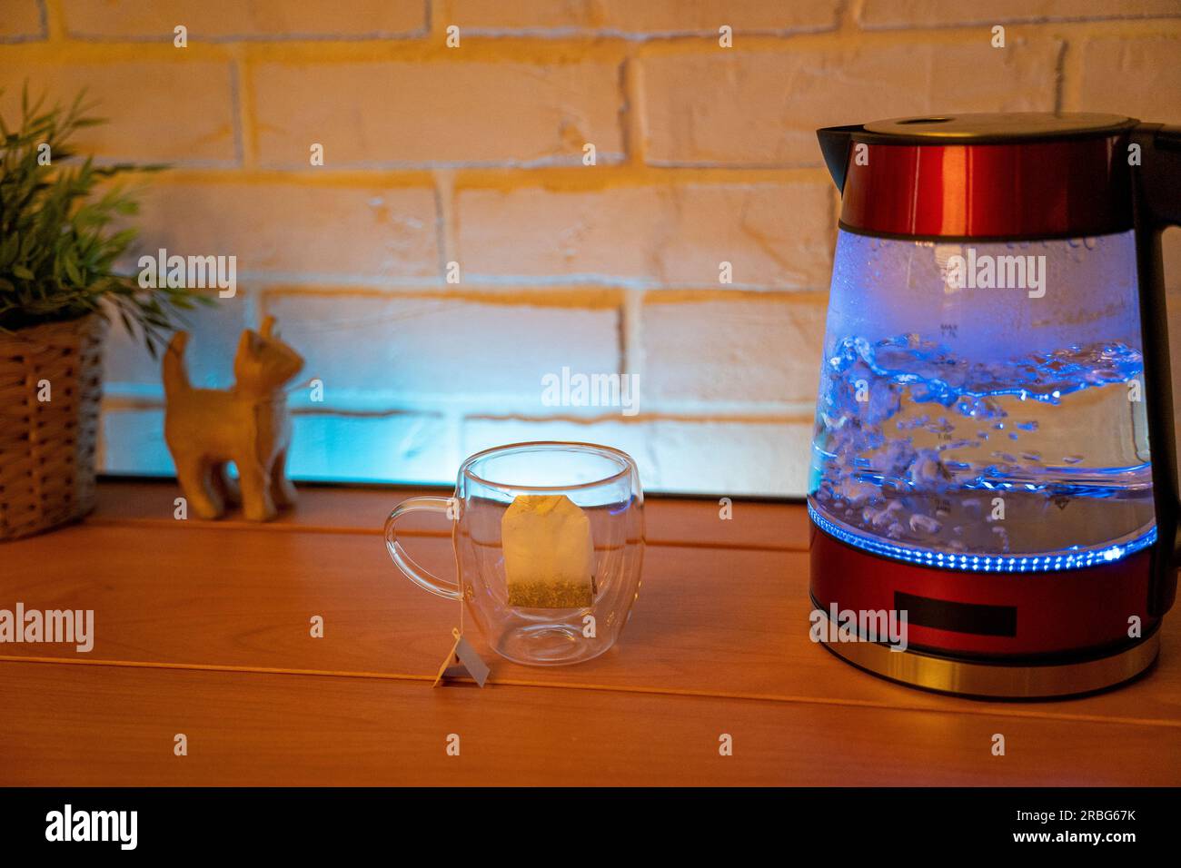 https://c8.alamy.com/comp/2RBG67K/a-glass-electric-kettle-on-a-wooden-table-and-a-transparent-mug-with-a-bag-of-delicious-tea-high-quality-photo-2RBG67K.jpg