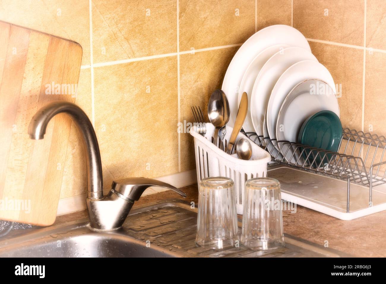 Washed plates, cutlery and glasses, drying in their racks close to the sink in the kitchen Stock Photo