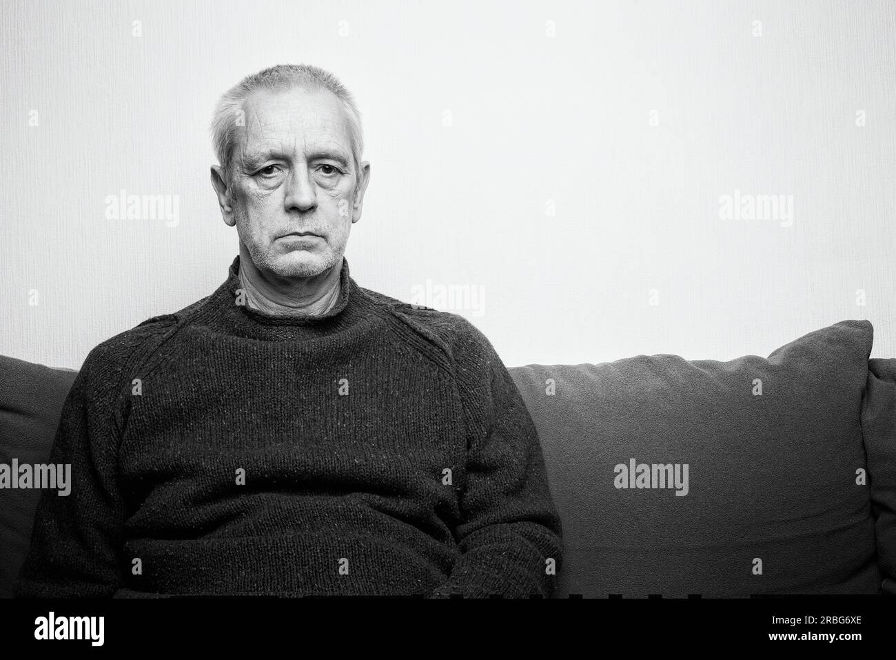 Dramatic portrait of a sad and depressed adult man sit on a sofa and looking into space with lackluster eyes. Negative space for copy text Stock Photo
