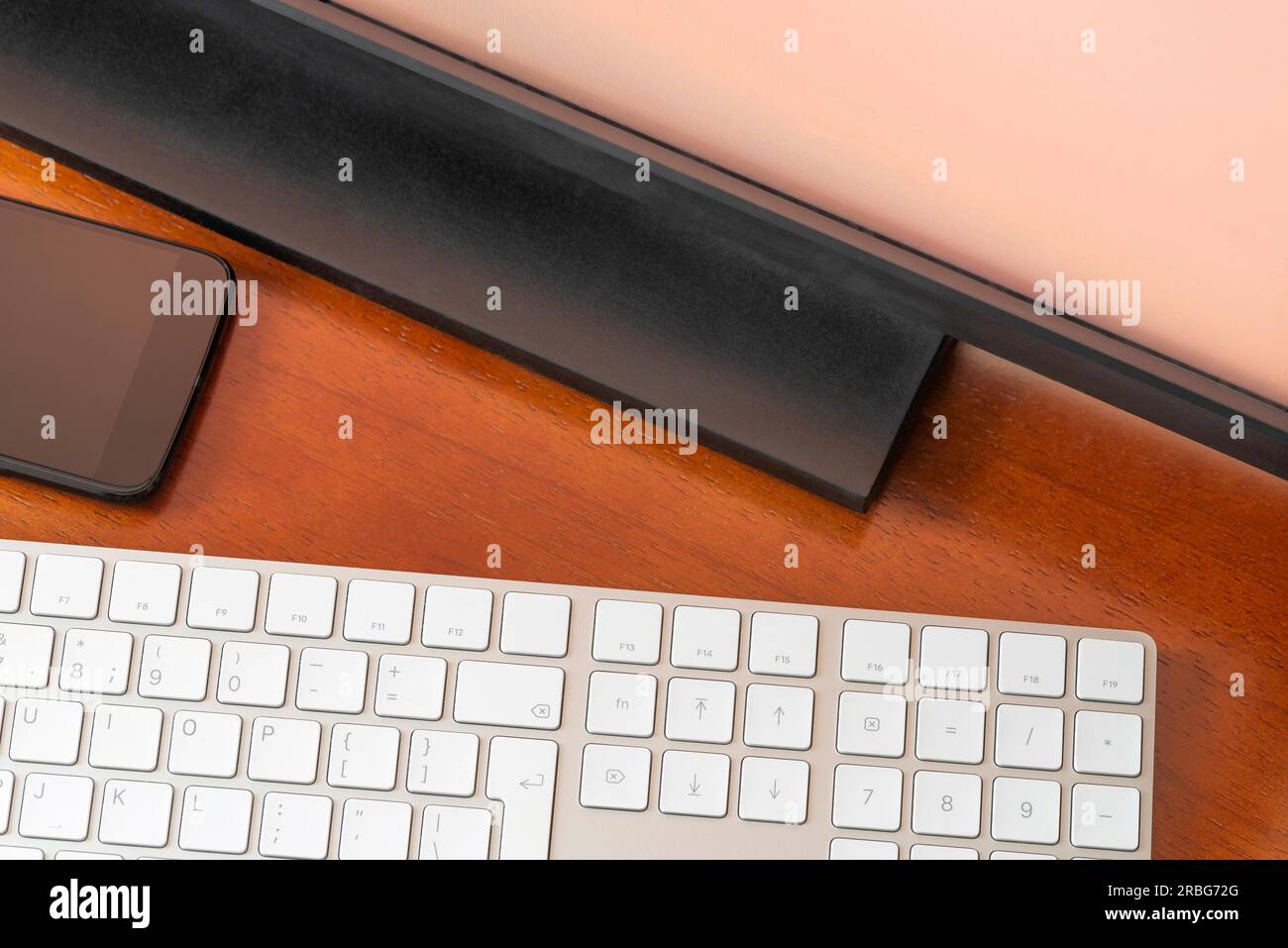 A computer monitor, a digital wireless keyboard and a black smartphone on a round wooden desk Stock Photo