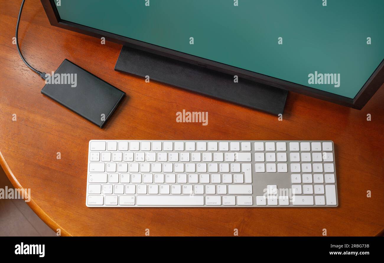 A computer monitor, a digital wireless keyboard and a hard disk drive on a round wooden desk Stock Photo
