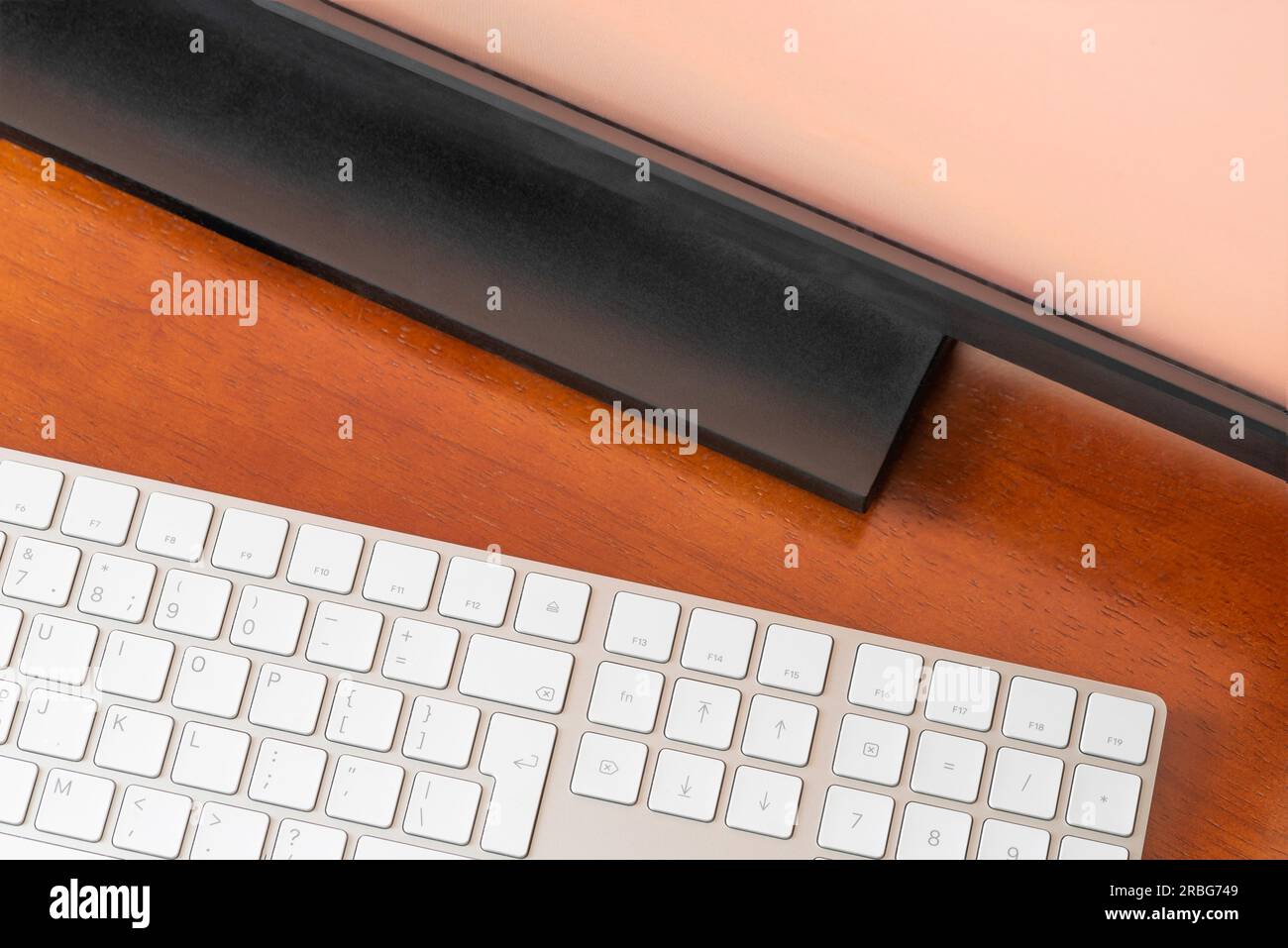A computer monitor and a white digital wireless keyboard on a round wooden desk Stock Photo