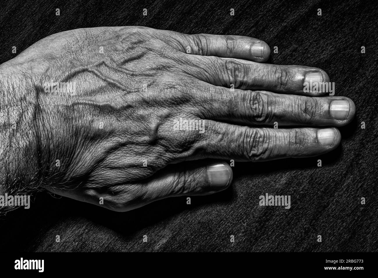 Black and White photo of a senior man left hand on dark background Stock Photo