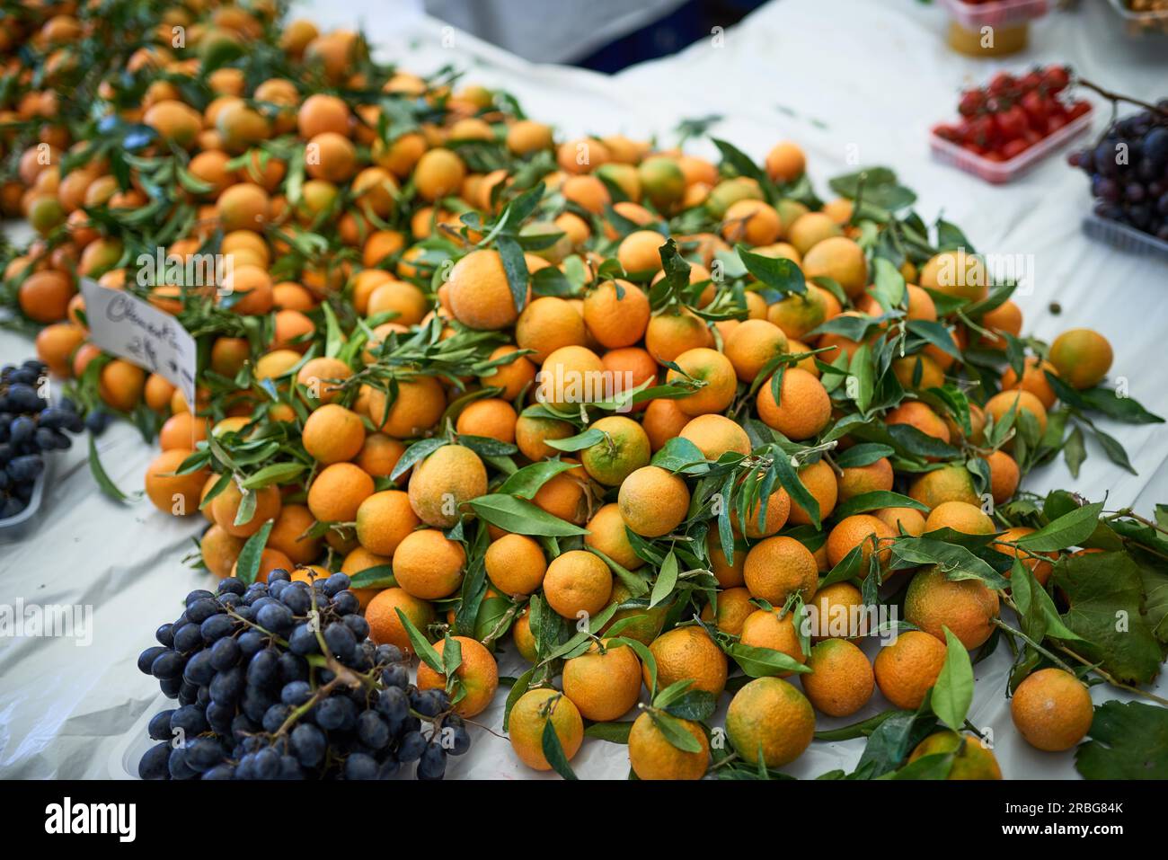 Fresh clementines with green leaves on sale at a farmers market or store piled high on a table Stock Photo