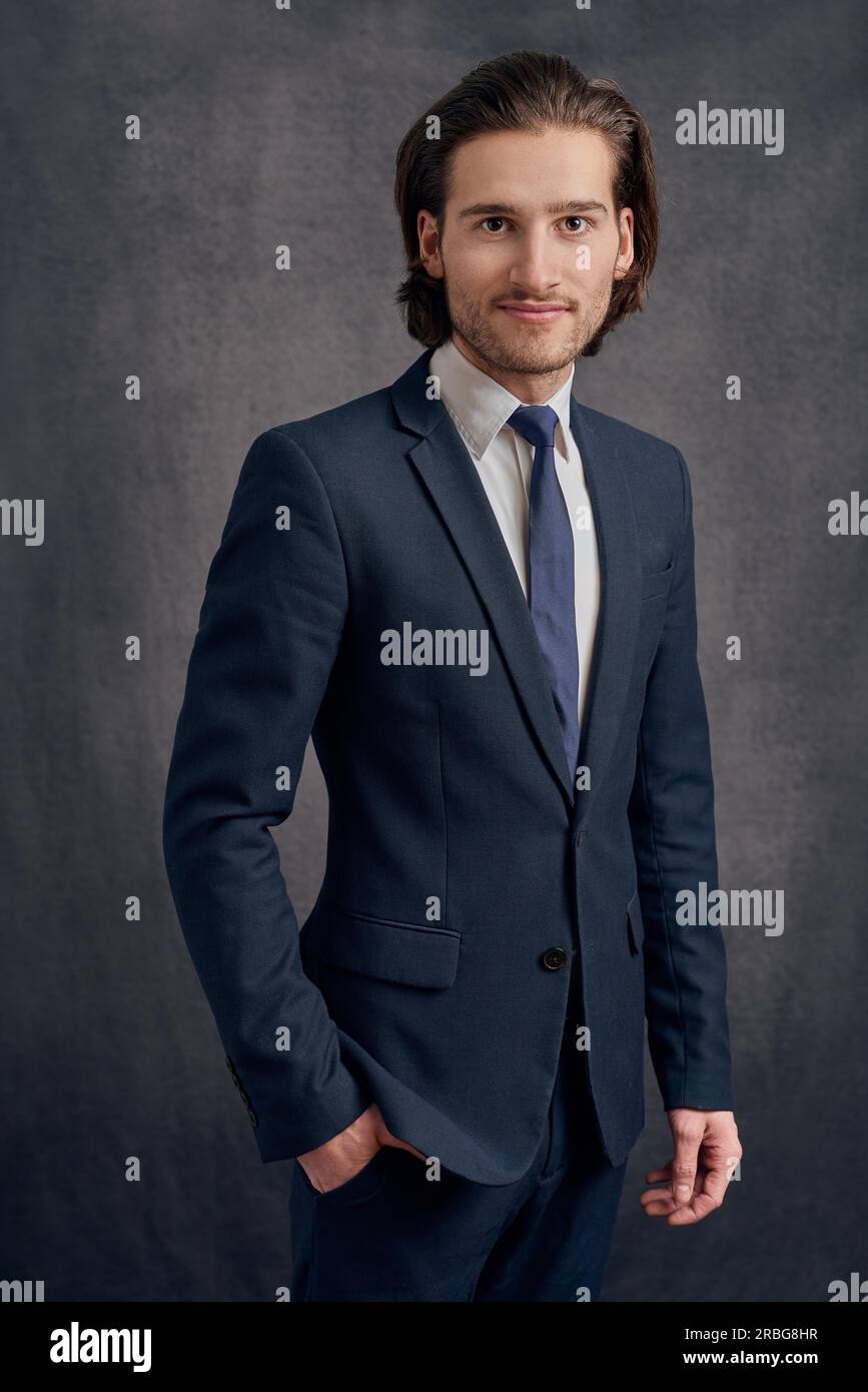 Handsome young man with long haircut in business suit with blue necktie, standing and looking at the camera Stock Photo