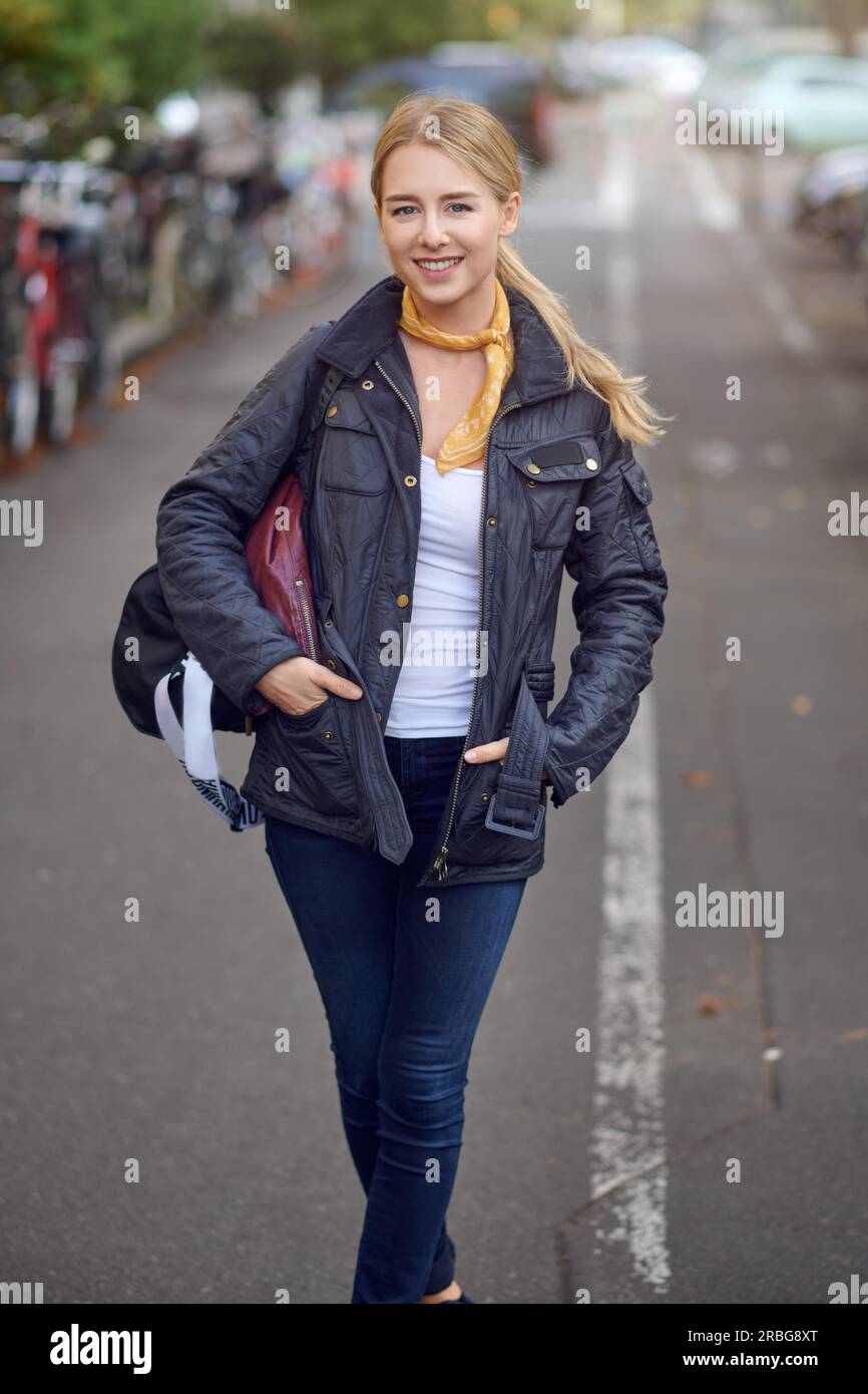 Portrait of young blond woman in city street, holding hands in her