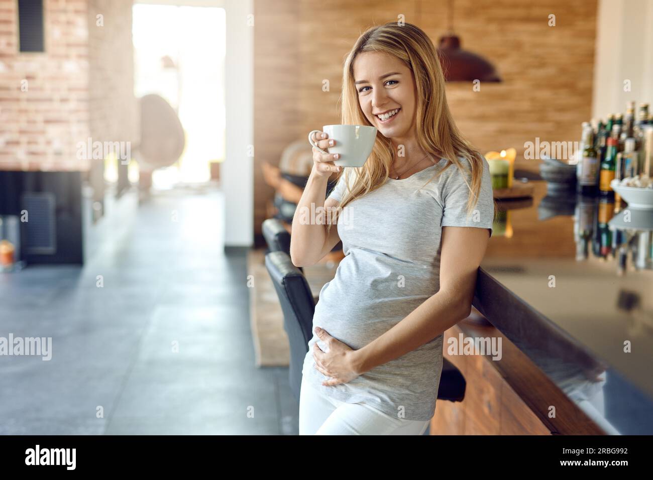Smiling happy young pregnant woman relaxing leaning against a bar ...