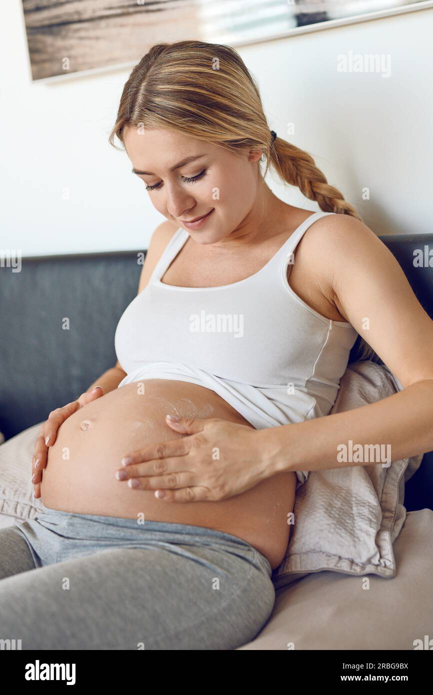 Young pregnant woman rubbing moisturising cream on her belly to moisturise her skin and reduce the possibility of stretch marks after childbirth Stock Photo