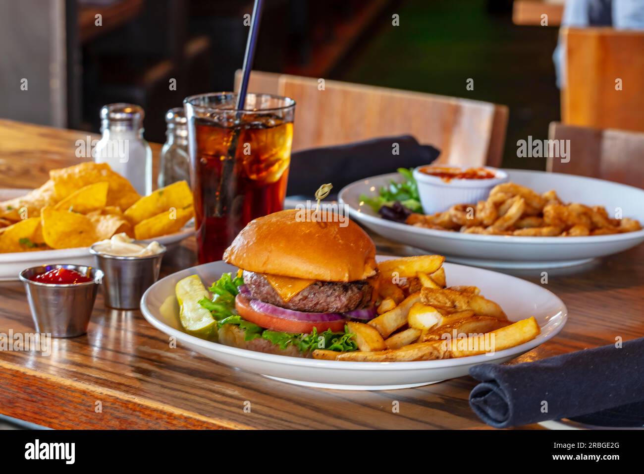 Home made hamburger with beef, onion, tomato, lettuce and cheese. Fresh burger closeup on wooden rustic table with potato fries, beer and chips. Stock Photo