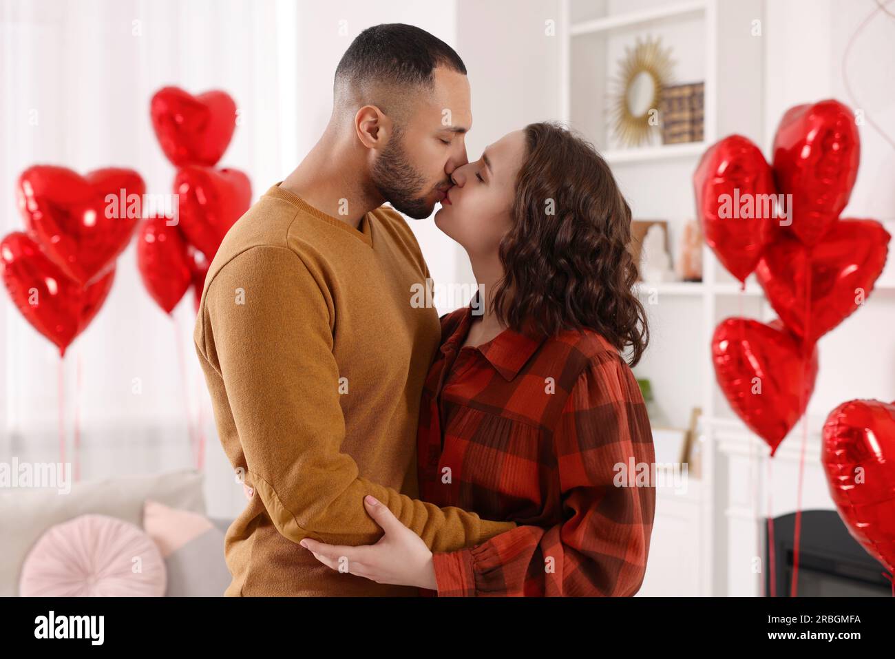 Lovely couple kissing in room decorated with heart shaped air balloons ...