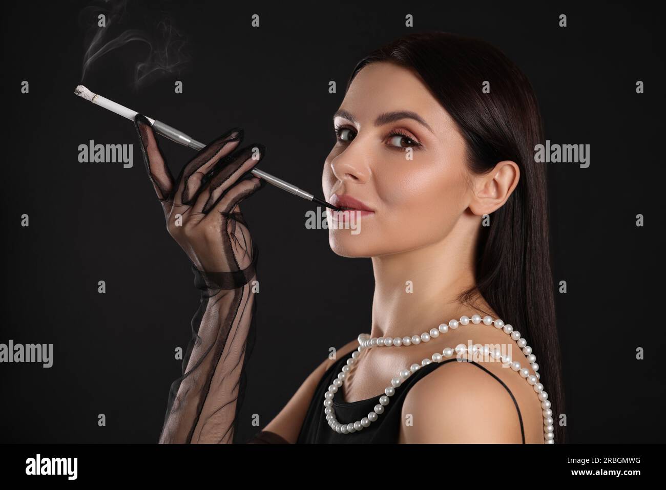 Woman using long cigarette holder for smoking on black background Stock  Photo