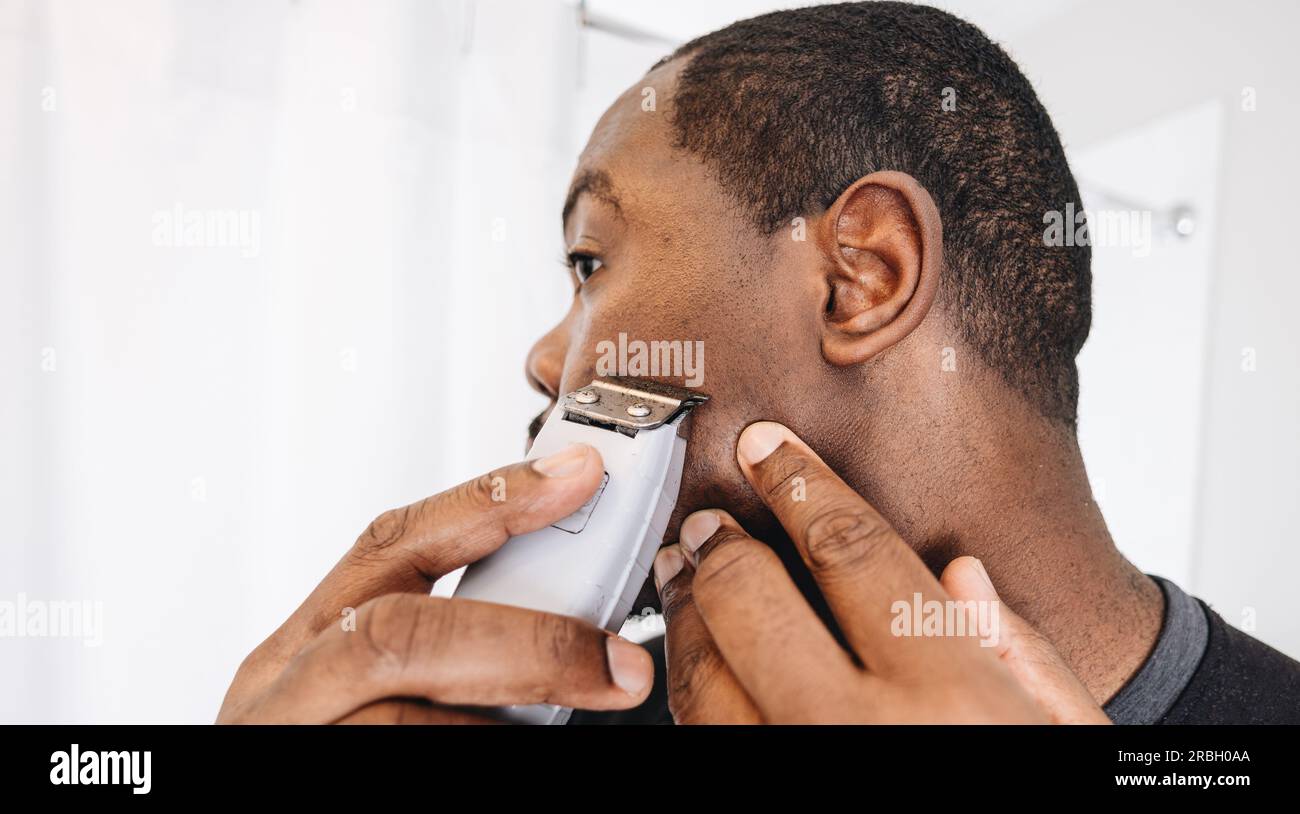 African American man at home in bathroom cutting hair with clippers