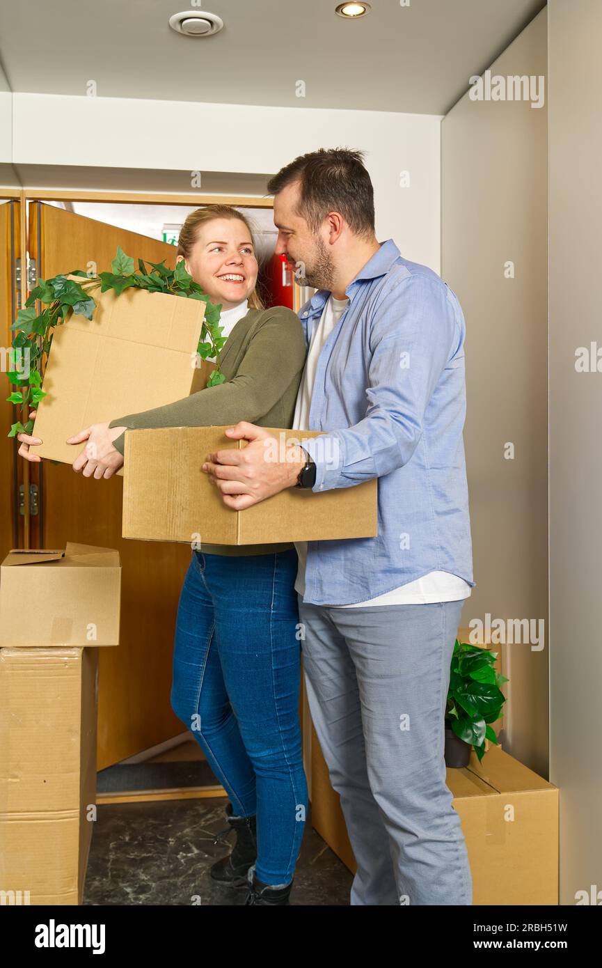 Happy couple moving in their new apartment carrying cardboard boxes ...
