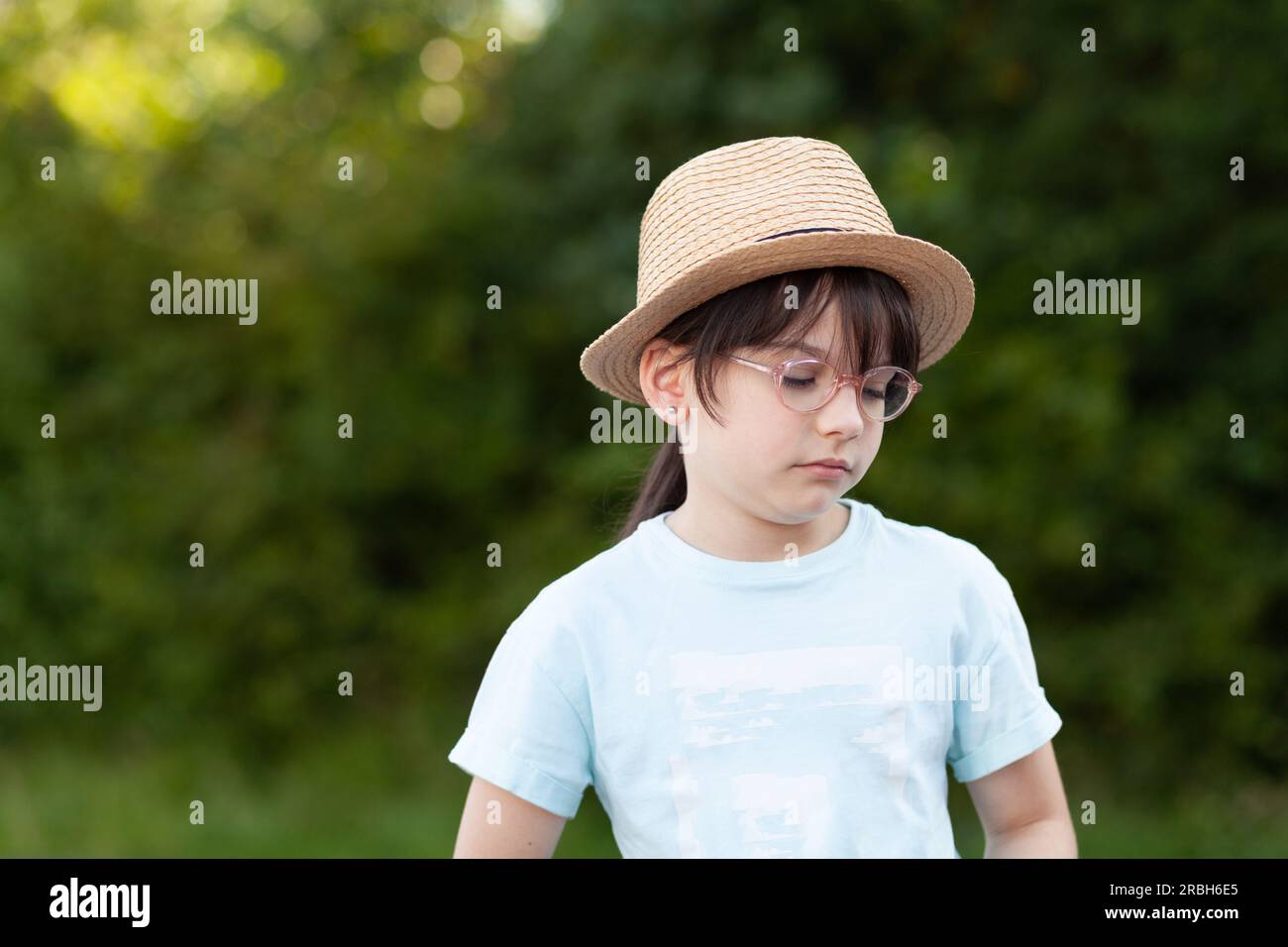 Cute little girl wearing a straw hat and glasses in the park Stock Photo