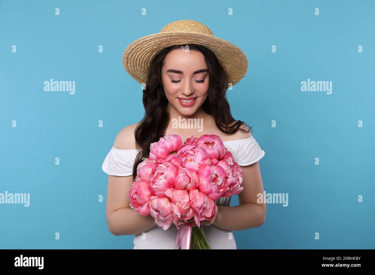 Beautiful young woman in straw hat with bouquet of pink peonies against ...