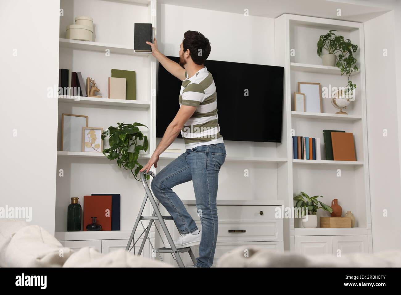 Man on metal folding ladder taking book from shelf at home Stock Photo ...