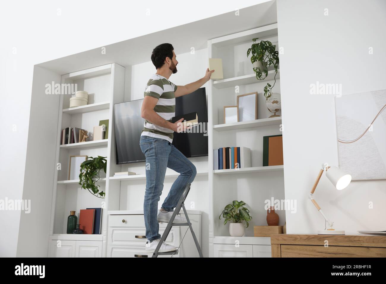 Man on metal folding ladder taking book from shelf at home Stock Photo ...