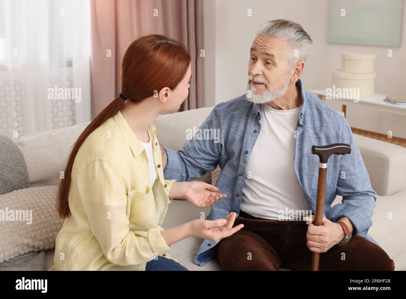 Caregiver and senior man with walking cane on sofa at home Stock Photo ...