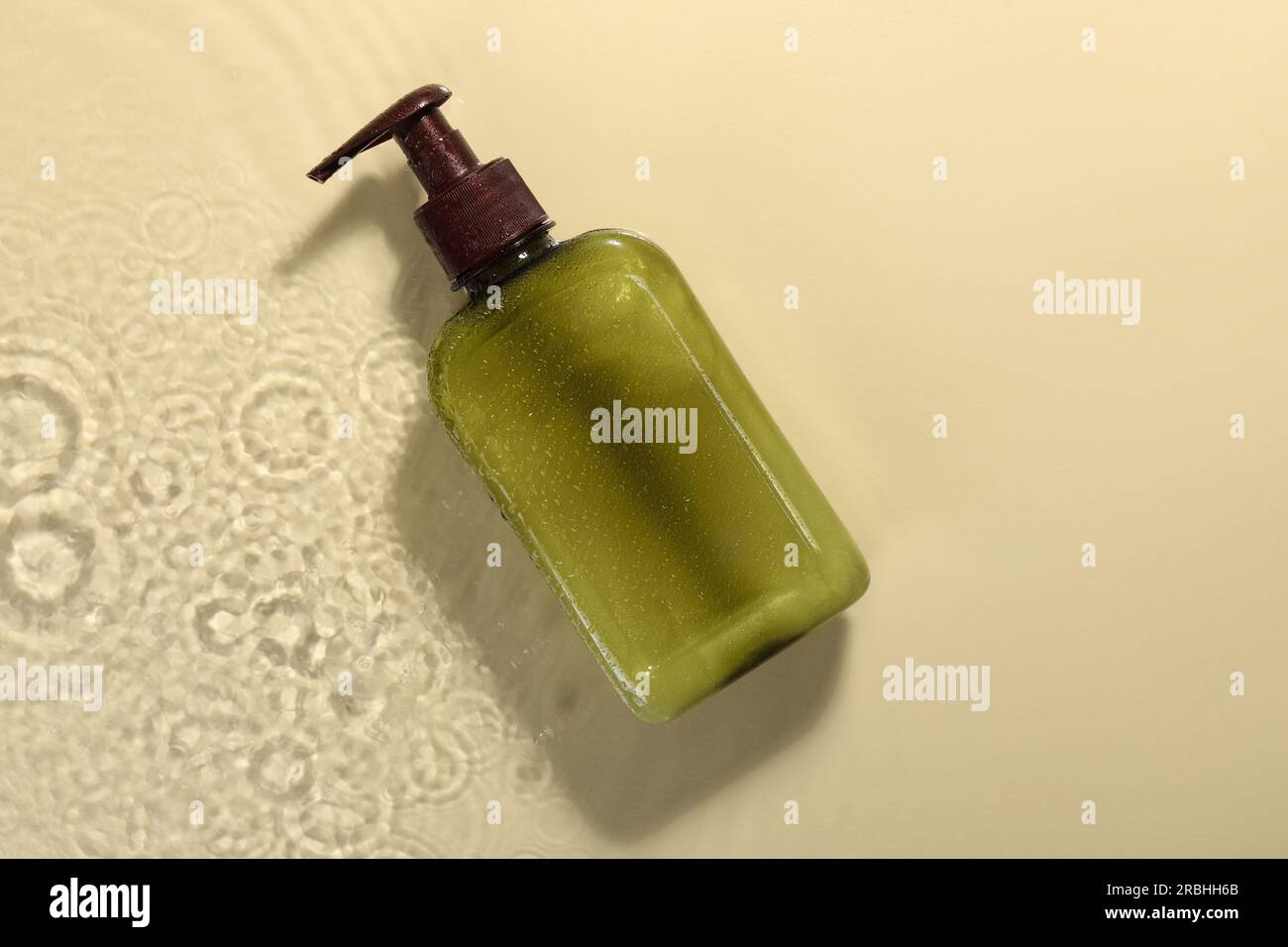 Bottle of face cleansing product in water against beige background, top