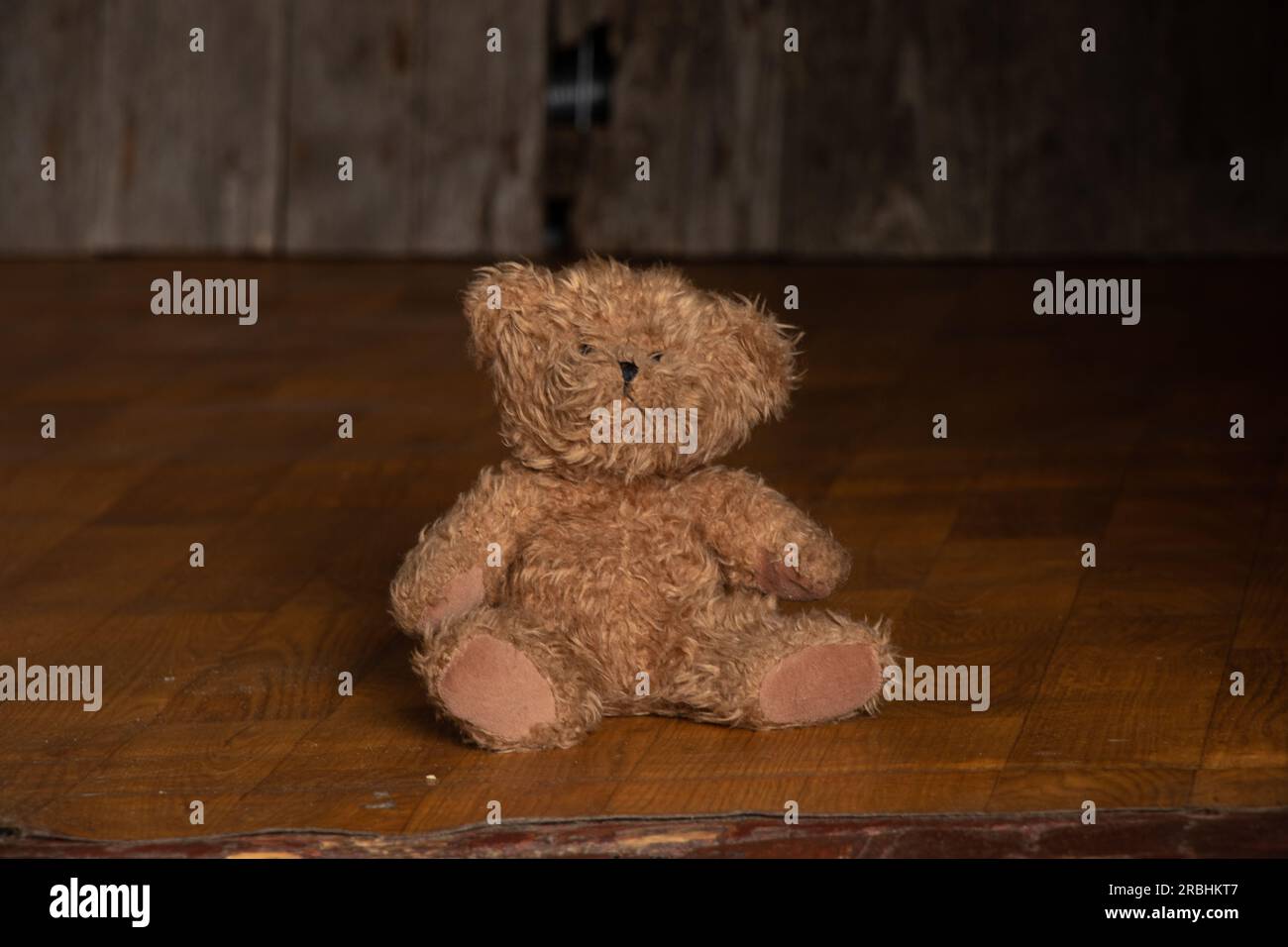 old dirty teddy bear lies on the floor in a dark room at home, abandoned and alone, poverty Stock Photo