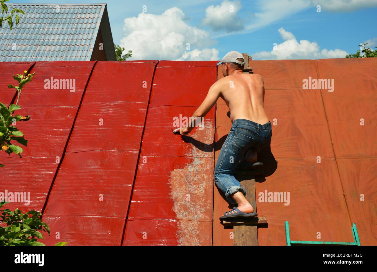 KYIV, UKRAINE MAY, 15, 2023 Roofer repainting old metal roof with a paint brush and red paint
