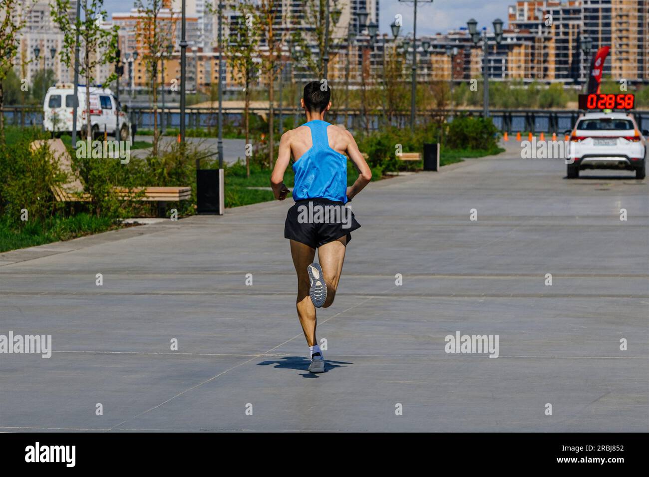 leading athlete runner running marathon race in park behind car time, summer sports event Stock Photo
