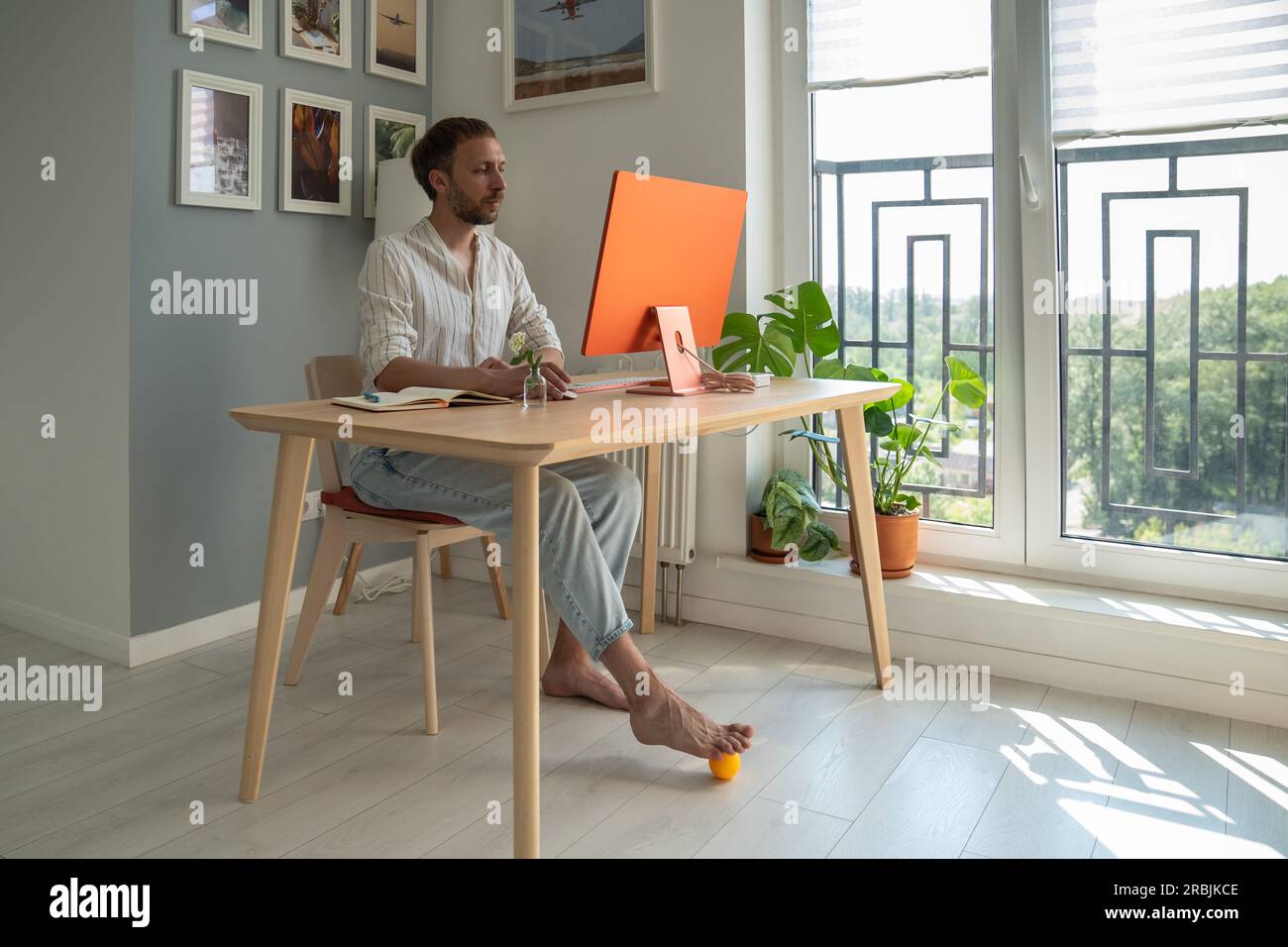 Young man freelancer using foot massager while sitting in front of computer Stock Photo