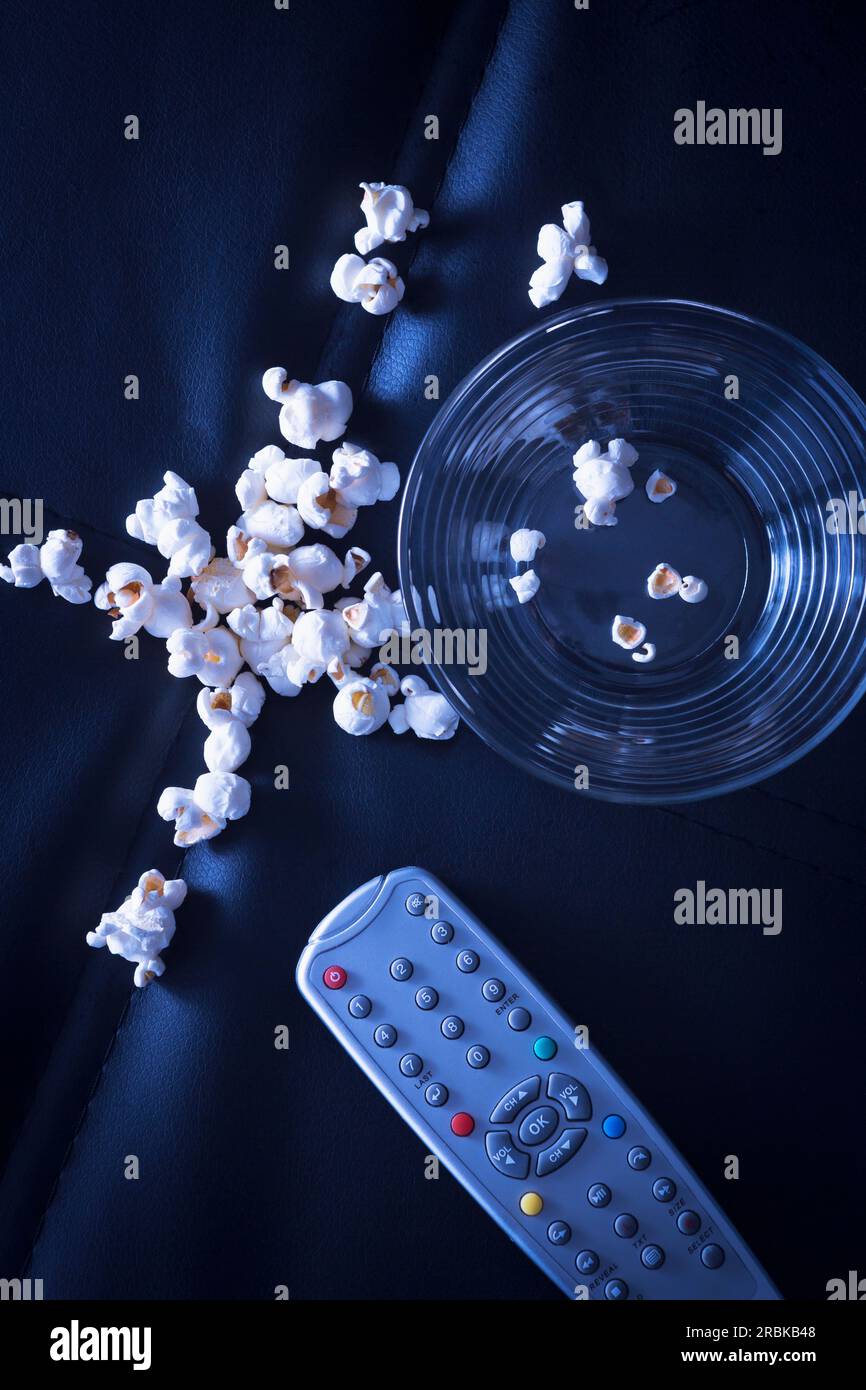 Bowl of popcorn and remote control on black couch in the evening Stock Photo