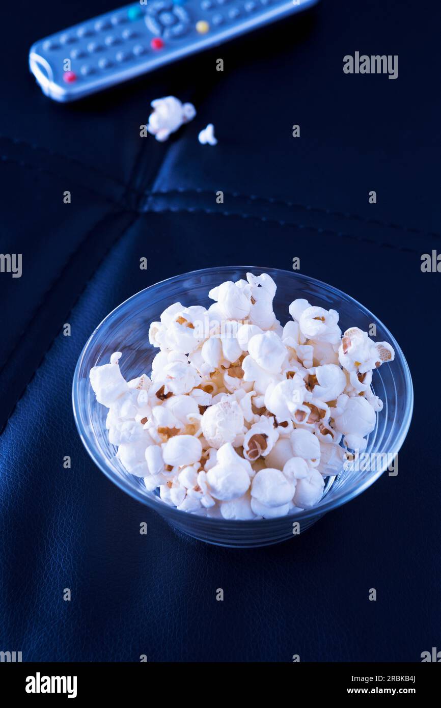 Bowl of popcorn and remote control  on black couch in the evening Stock Photo