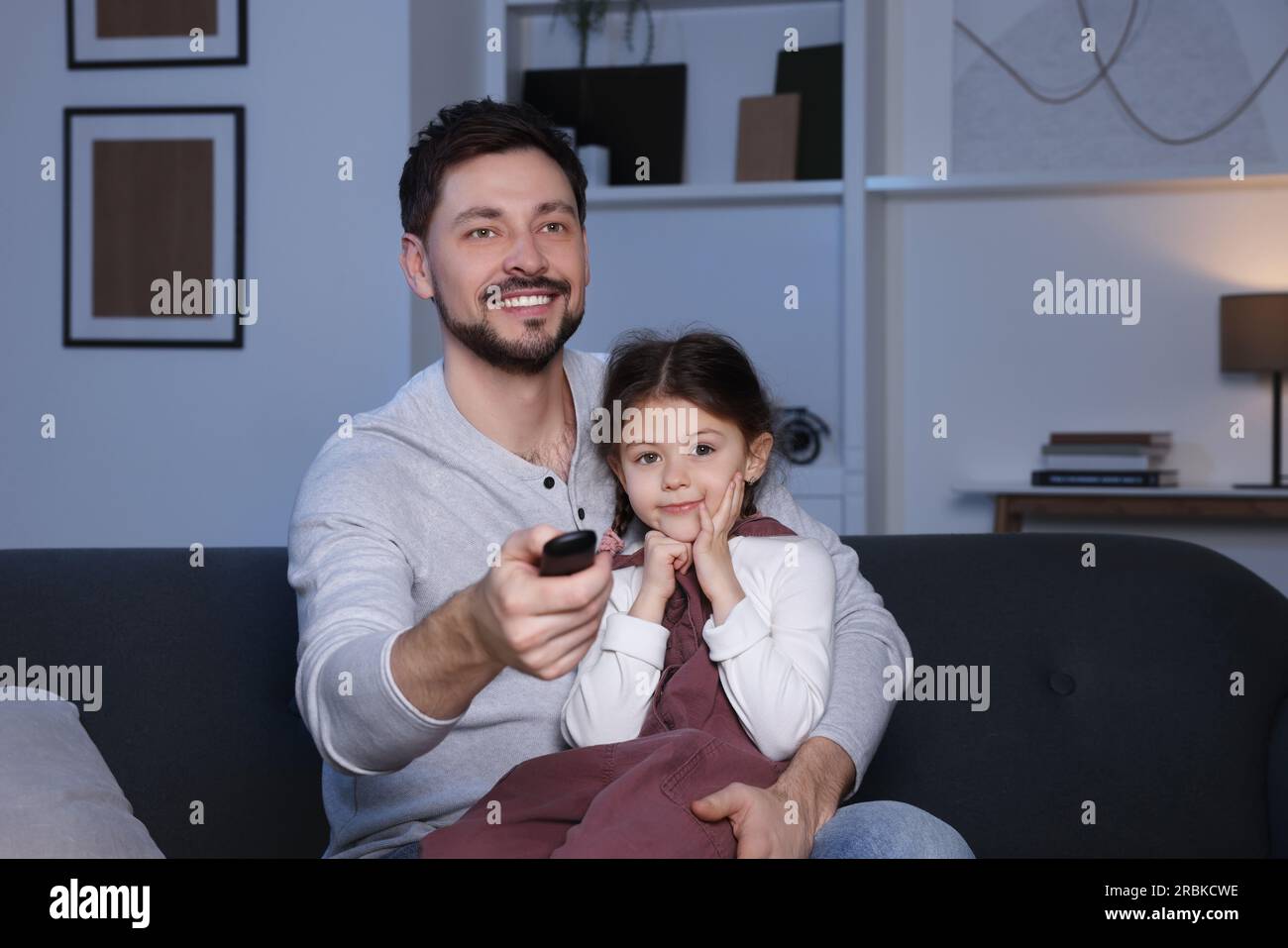 Father and daughter at home. Happy man changing TV channels with remote ...