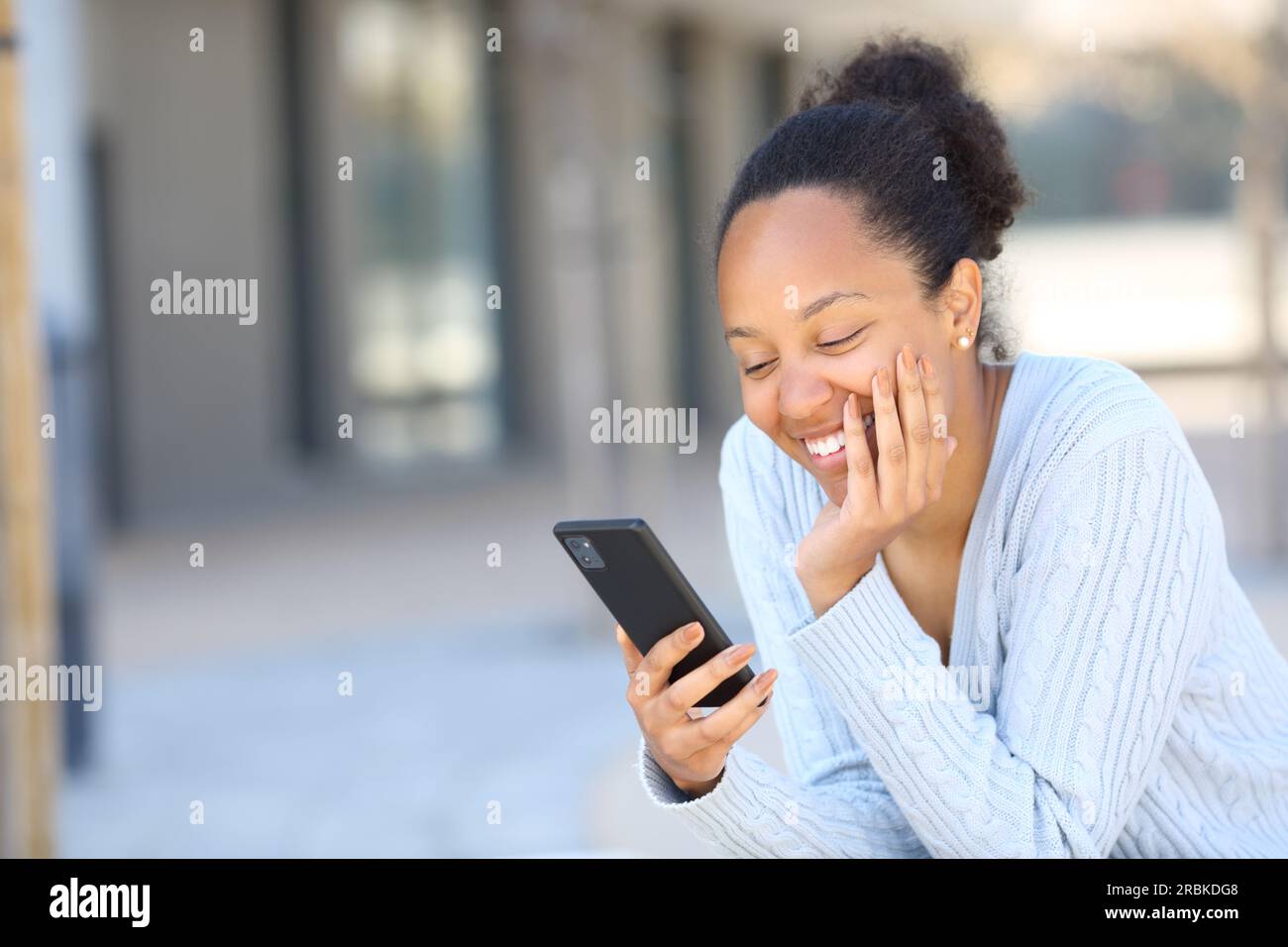 Happy black woman laughing using phone in the street Stock Photo - Alamy