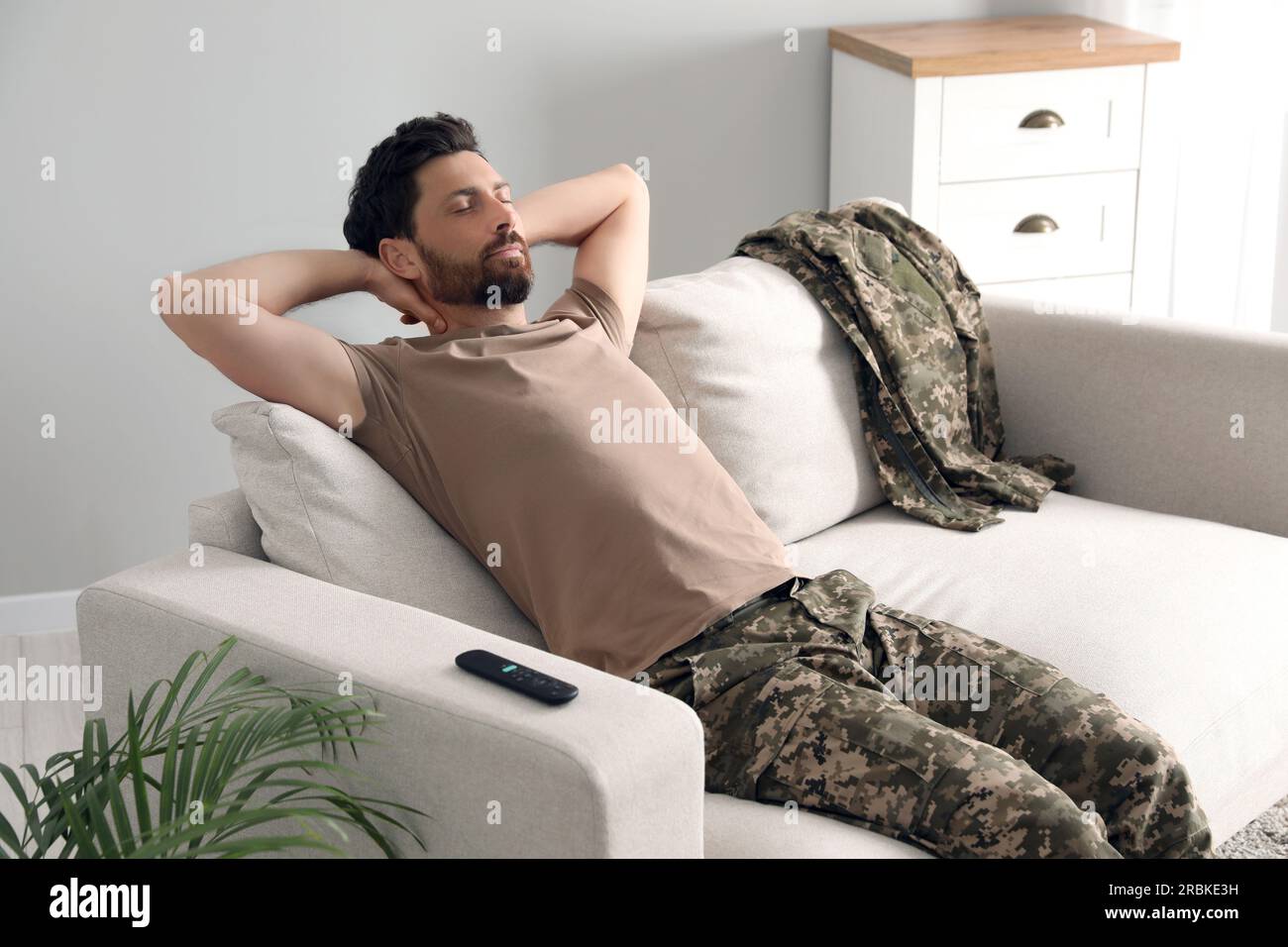 Soldier napping on soft sofa in living room. Military service Stock