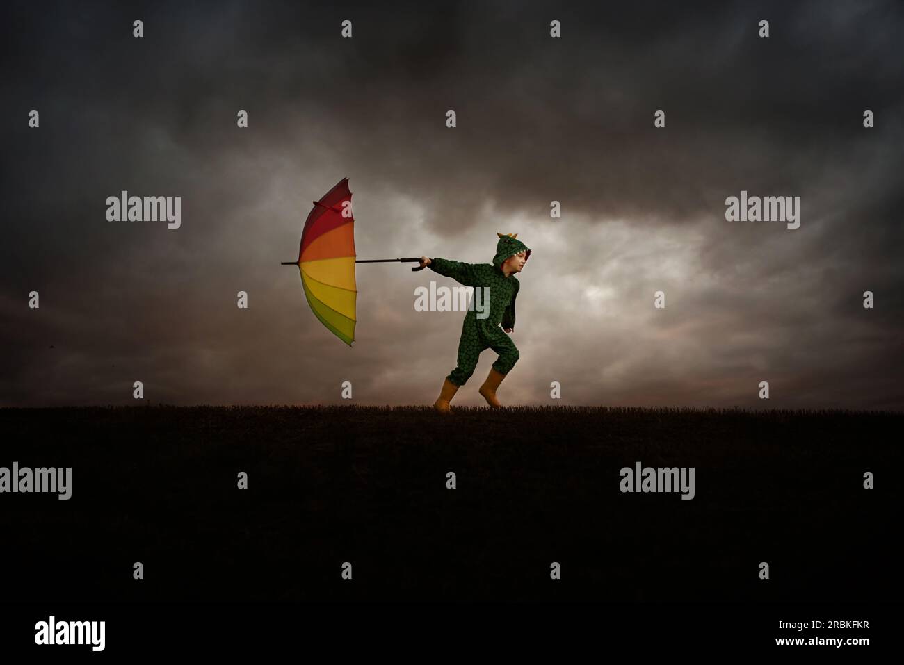 5 year old boy in dinosaur pyjamas and rainbow umbrella Stock