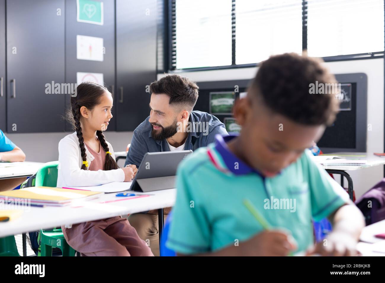 Happy male teacher and schoolgirl using tablet at her desk in diverse ...