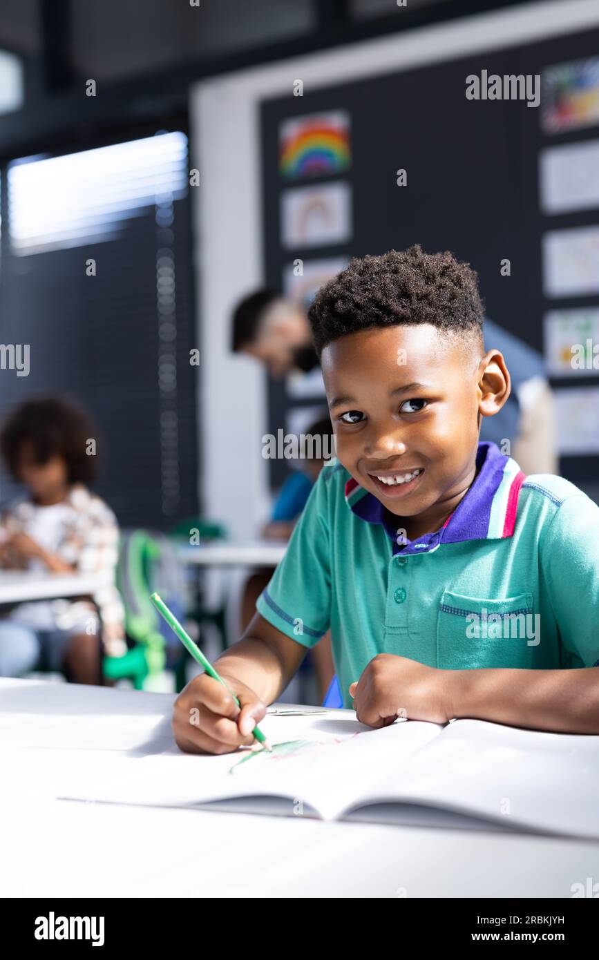 Vertical of happy african american schoolboy at desk in elementary ...