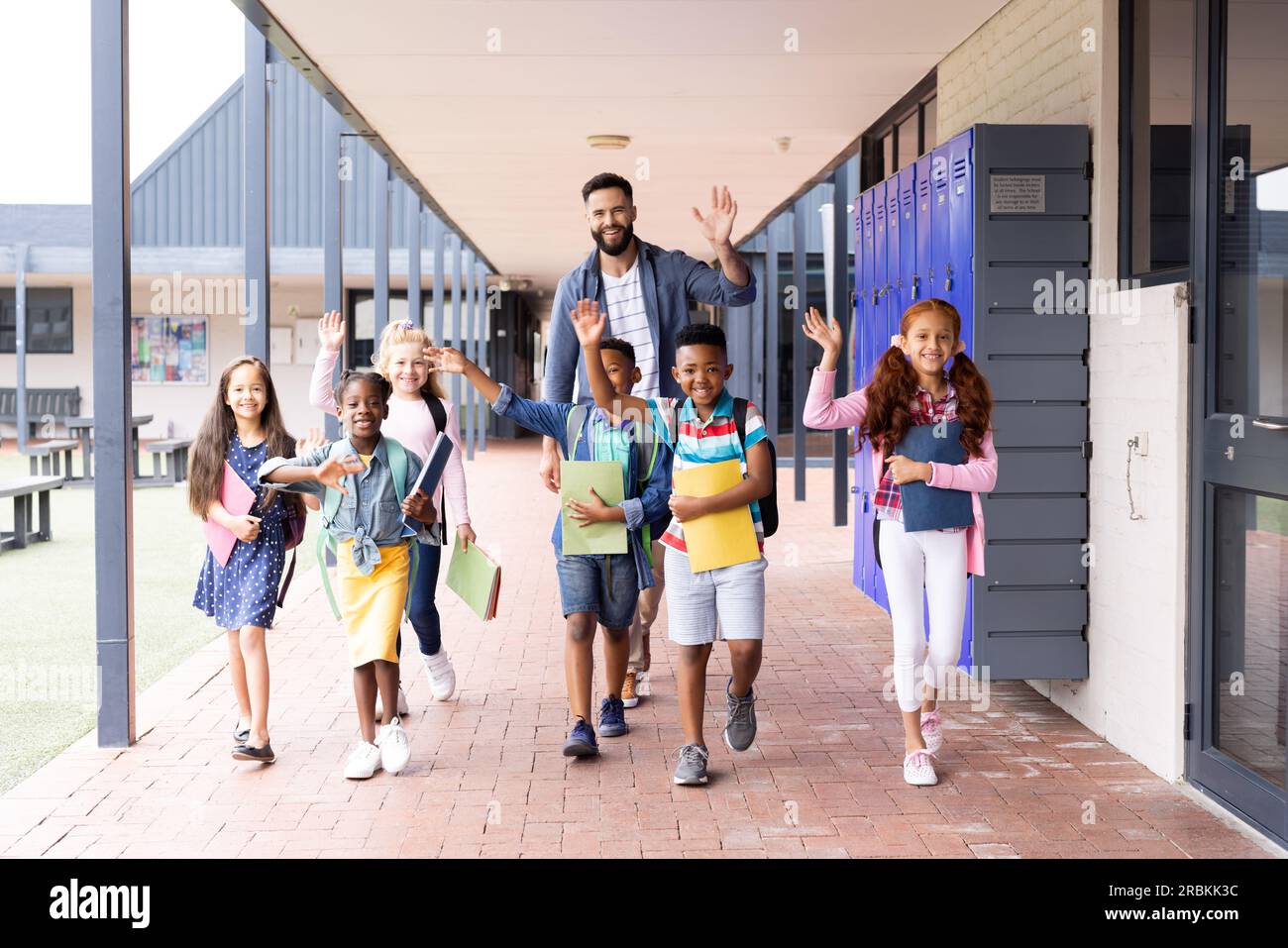 Diverse, happy male teacher and elementary schoolchildren waving in ...