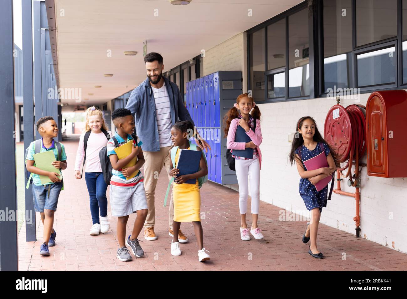 Diverse, happy male teacher and elementary schoolchildren walking in ...