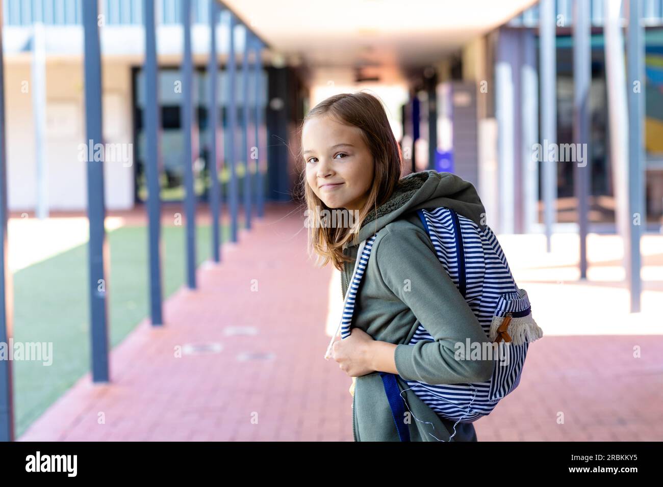Portrait of caucasian schoolgirl with schoolbag smiling to camera in school corridor Stock Photo