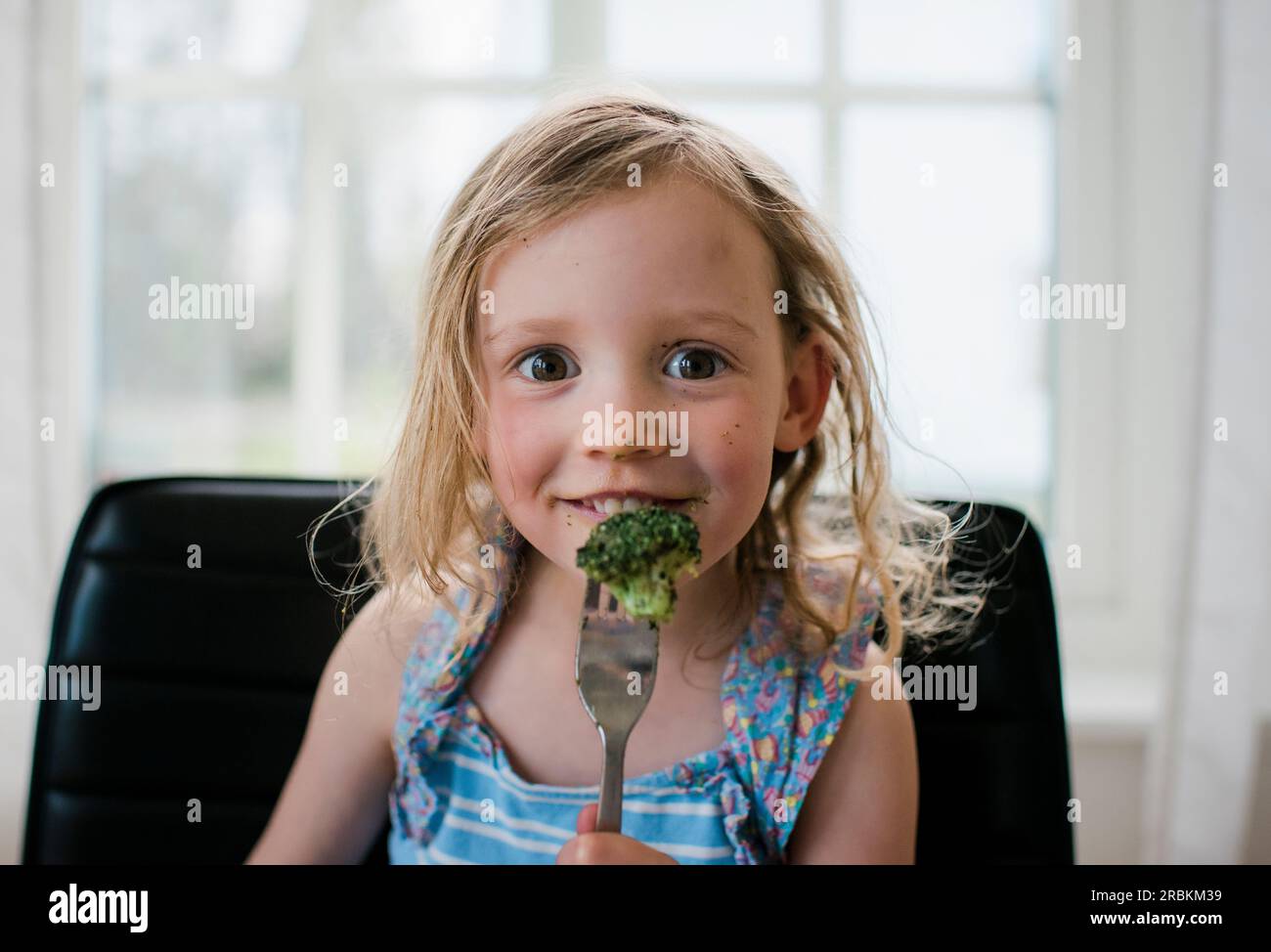 young girl eating broccoli at home with a messy face Stock Photo Alamy