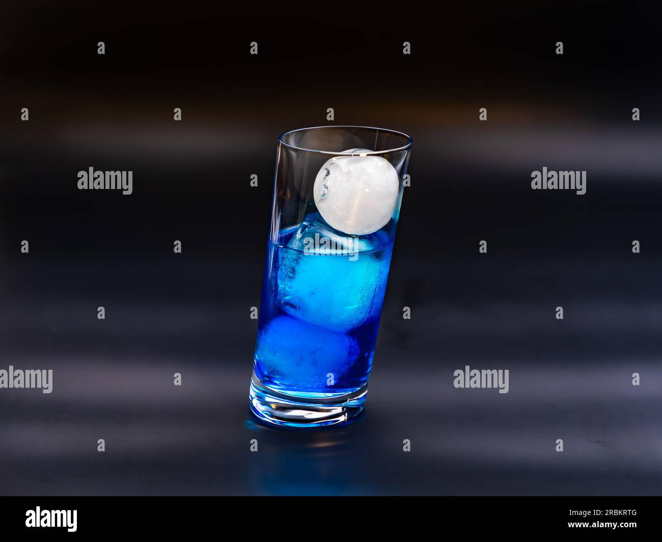 A blue long drink with ice in a slanted glass in the studio in front of a black background Stock Photo